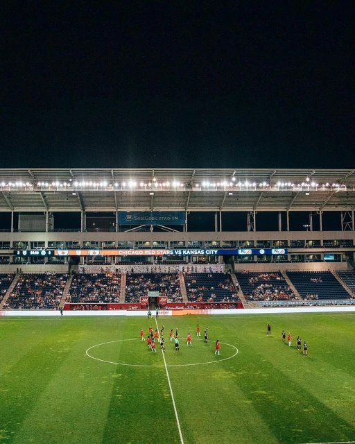 Wide shot of a soccer field at night with two teams lined up on the field during a match, stadium lights illuminate the scene.