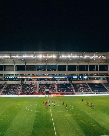 Wide shot of a soccer field at night with two teams lined up on the field during a match, stadium lights illuminate the scene.