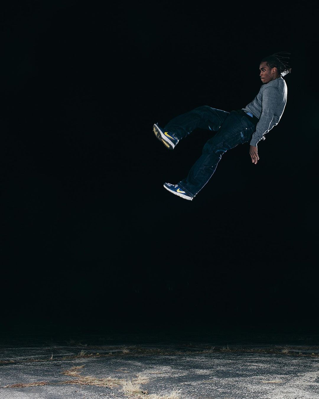 Athletic black man mid-air, captured in a dynamic outdoor shot, illuminated against a dark backdrop, showcasing movement and modern casual wear.