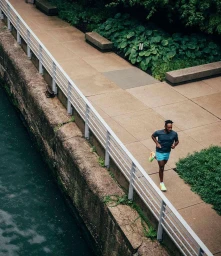 High-angle view of a man running along a paved waterfront path next to a white railing in Chicago by Thomas Chadwick.