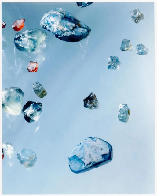 Scattered translucent gemstones with blue and red hues are displayed against a light blue background, suggesting a collection or raw materials.