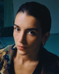 Close-up portrait of a woman with dark slicked-back hair wearing a patterned jacket in Paris by Thomas Chene.