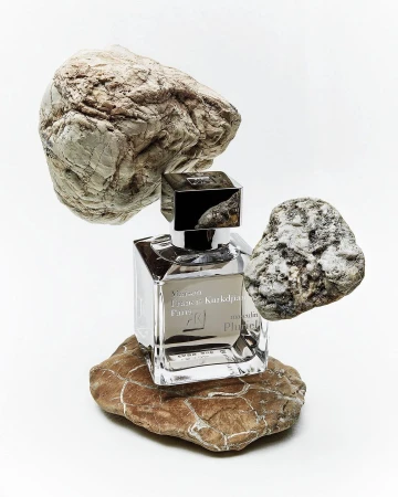 Square glass perfume bottle balanced among raw natural stones against a seamless white background.