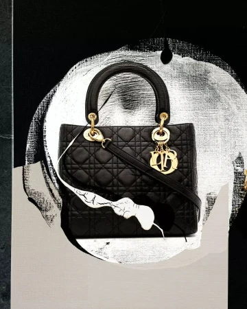 Fashion still life of a black quilted handbag with gold hardware on an abstract black and silver background.