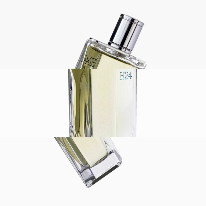 Angled studio shot of a transparent glass perfume bottle with a silver cap against a white background, showcasing minimalist product design.