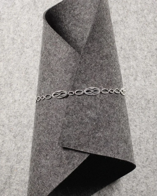 Silver chain with repeating infinity symbol links on folded grey felt fabric. Jewelry product shot showcases the necklace and material texture.