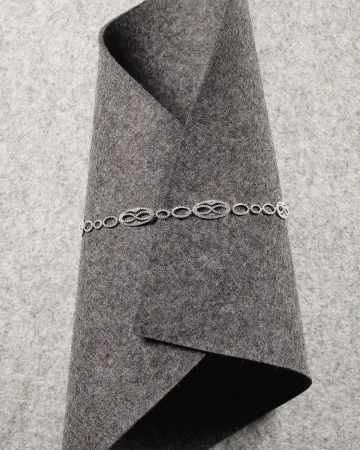 Silver chain with repeating infinity symbol links on folded grey felt fabric. Jewelry product shot showcases the necklace and material texture.