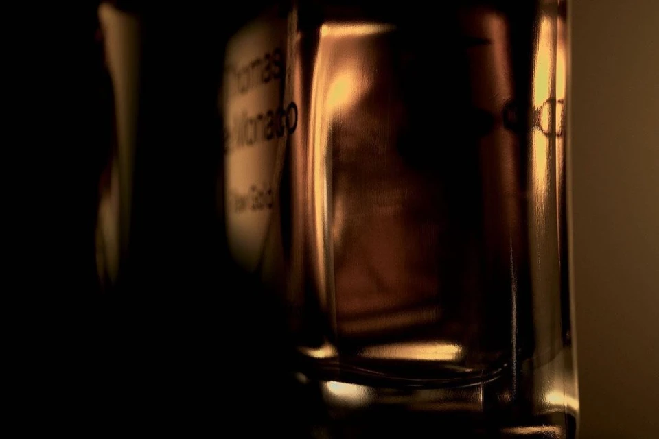 Close-up studio shot of a translucent perfume bottle with text on its label, set against a dark gold gradient background.