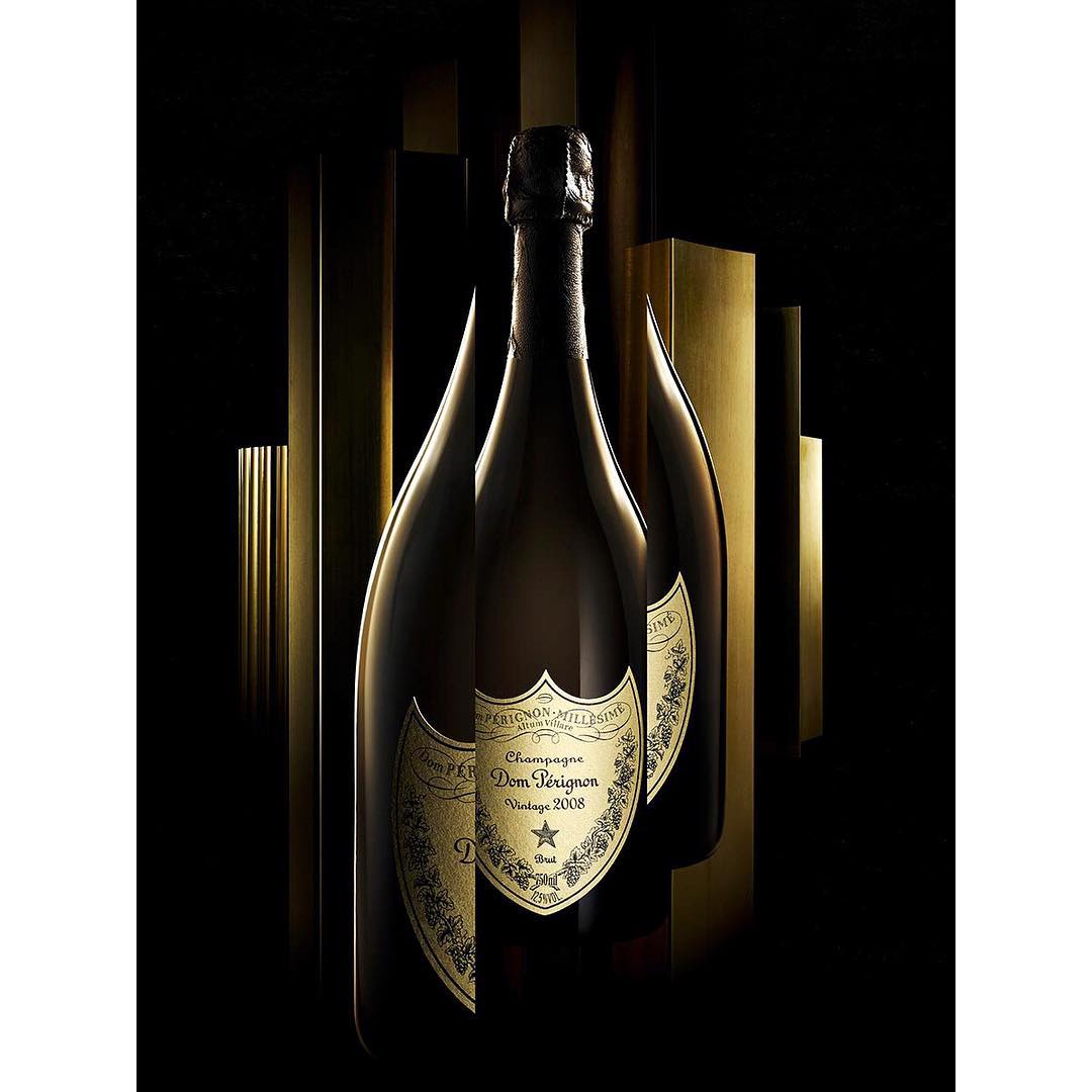 Three wine bottles are displayed against a backdrop of gold and black vertical bars, illuminated by directed light.