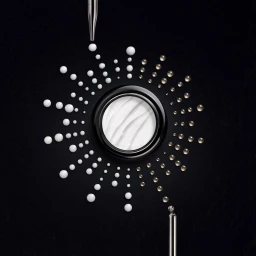 Top-down view of a round cosmetic jar surrounded by radiating white cream droplets and translucent beads against a dark background.