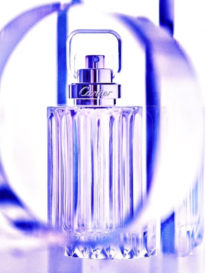 Crystal perfume bottle with silver accents sits in front of a decorative blue ribbon on a white surface in a beauty product shot.