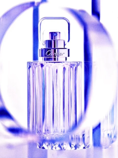 Crystal perfume bottle with silver accents sits in front of a decorative blue ribbon on a white surface in a beauty product shot.