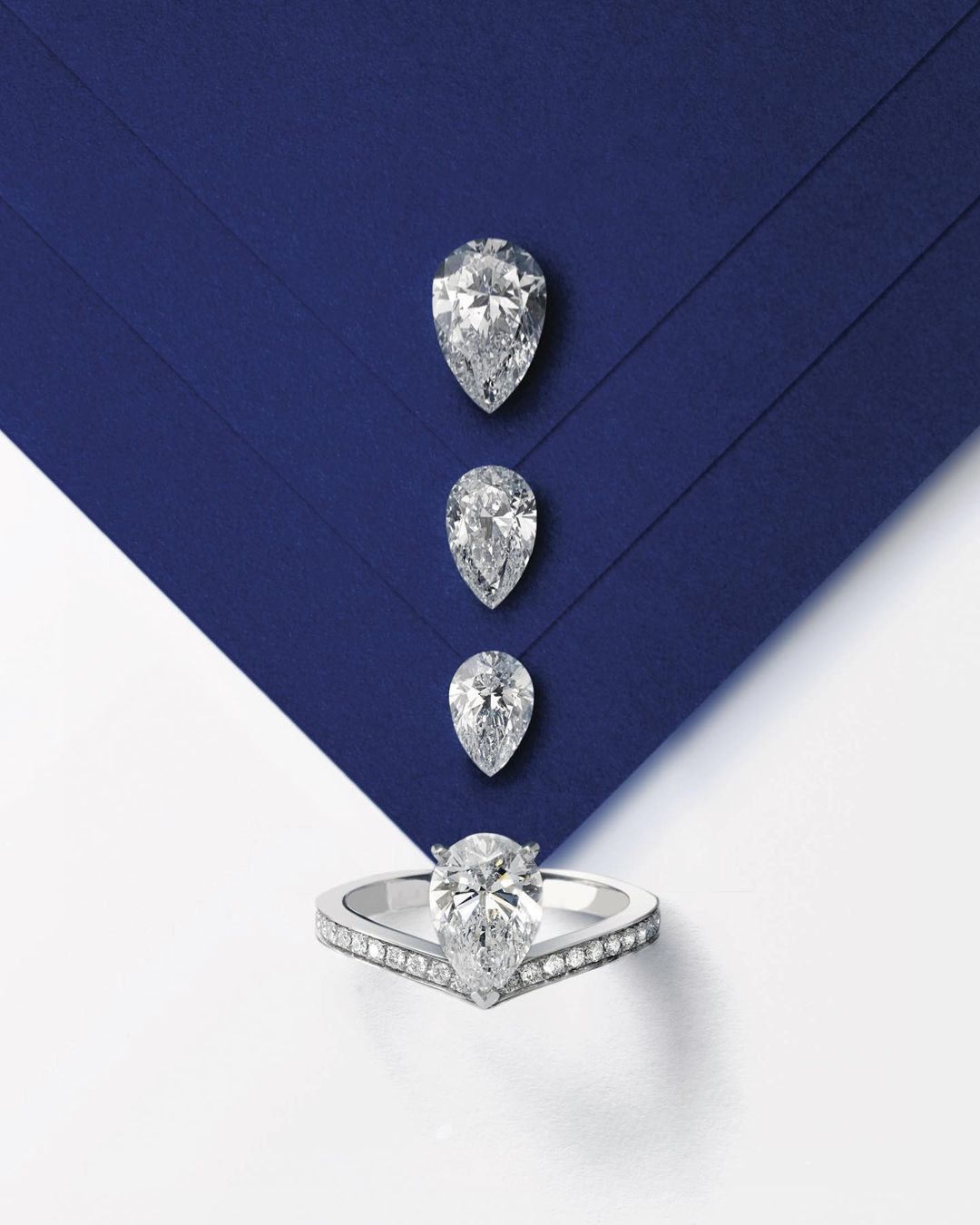 Engagement ring and loose diamonds on a blue background. The ring features a large, pear-shaped diamond surrounded by smaller diamonds.