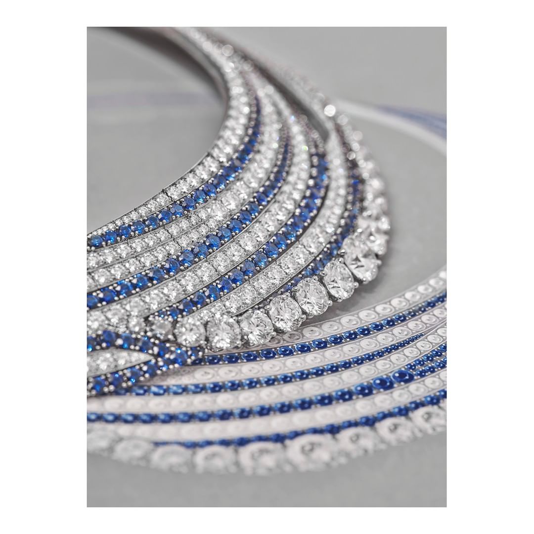 Close-up of a white gold necklace featuring diamonds and sapphires, laid flat against a neutral gray backdrop in a studio setting.
