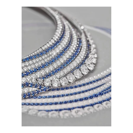 Close-up of a white gold necklace featuring diamonds and sapphires, laid flat against a neutral gray backdrop in a studio setting.