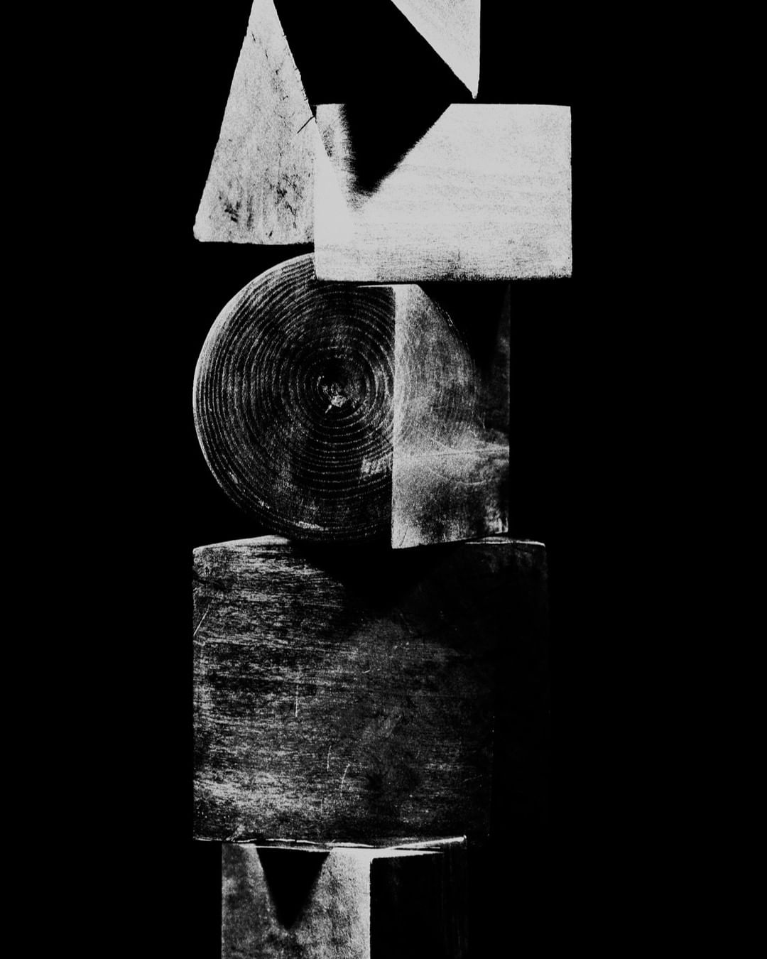 Abstract black and white still life of geometric wood blocks stacked vertically against a dark background in a studio setting.
