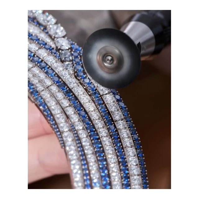 Close-up of a jeweler using a polishing tool on a diamond and sapphire necklace or bracelet, showcasing a fine jewelry making process.