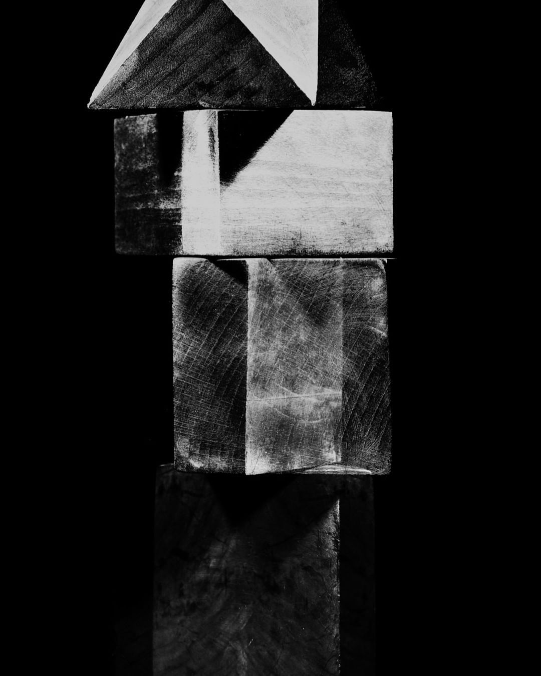 Monochrome photograph of stacked wooden blocks creates an abstract geometric composition against a black background with subtle reflections.