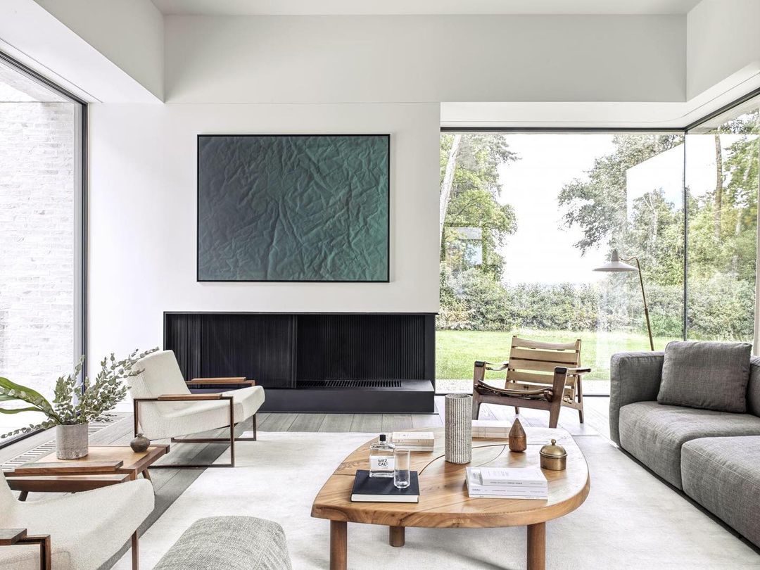 Living room interior with a grey sofa, wooden coffee table, two armchairs, a black fireplace, and a large abstract art piece.