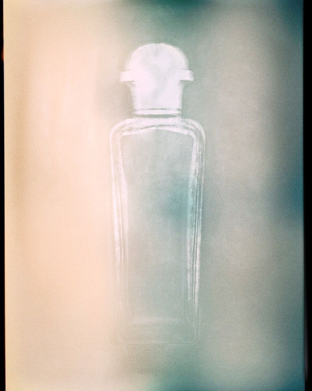 Elegant glass bottle with white cap set against blurred beige and grey background in studio lighting, showcasing minimalism.