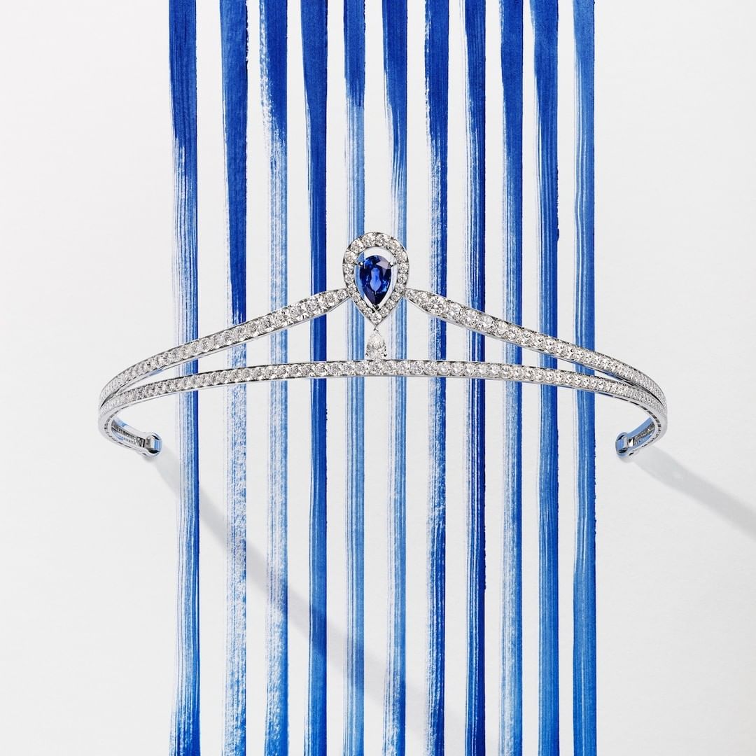Elegant diamond tiara with blue sapphire teardrop gem on a white background with blue painted stripes. Formal jewellery, headpiece.
