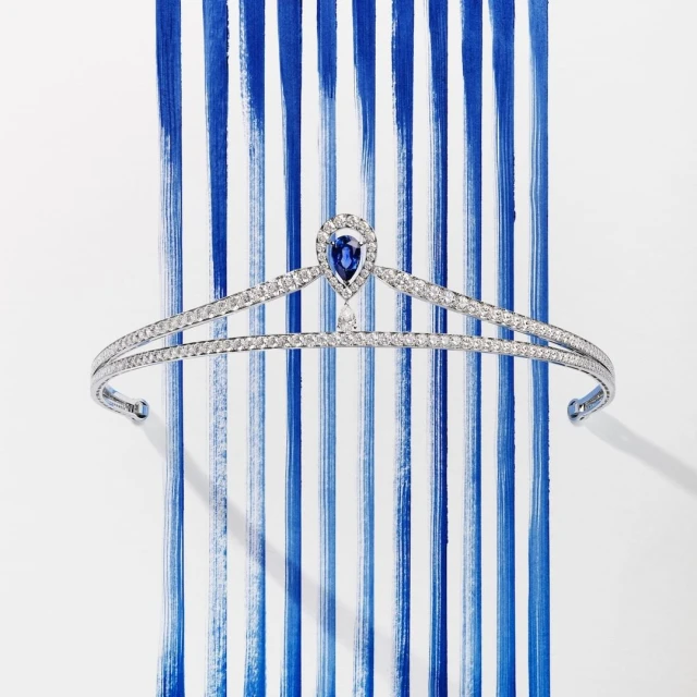 Elegant diamond tiara with blue sapphire teardrop gem on a white background with blue painted stripes. Formal jewellery, headpiece.