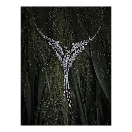 Close-up of a sparkling diamond necklace with leaf-like patterns on a bed of green grasses. Jewellery advertisement or product photography.