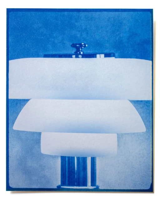 Blue-toned still life photograph of a modern lamp composed of white, tiered shades and a chrome base and knob against a blue background.