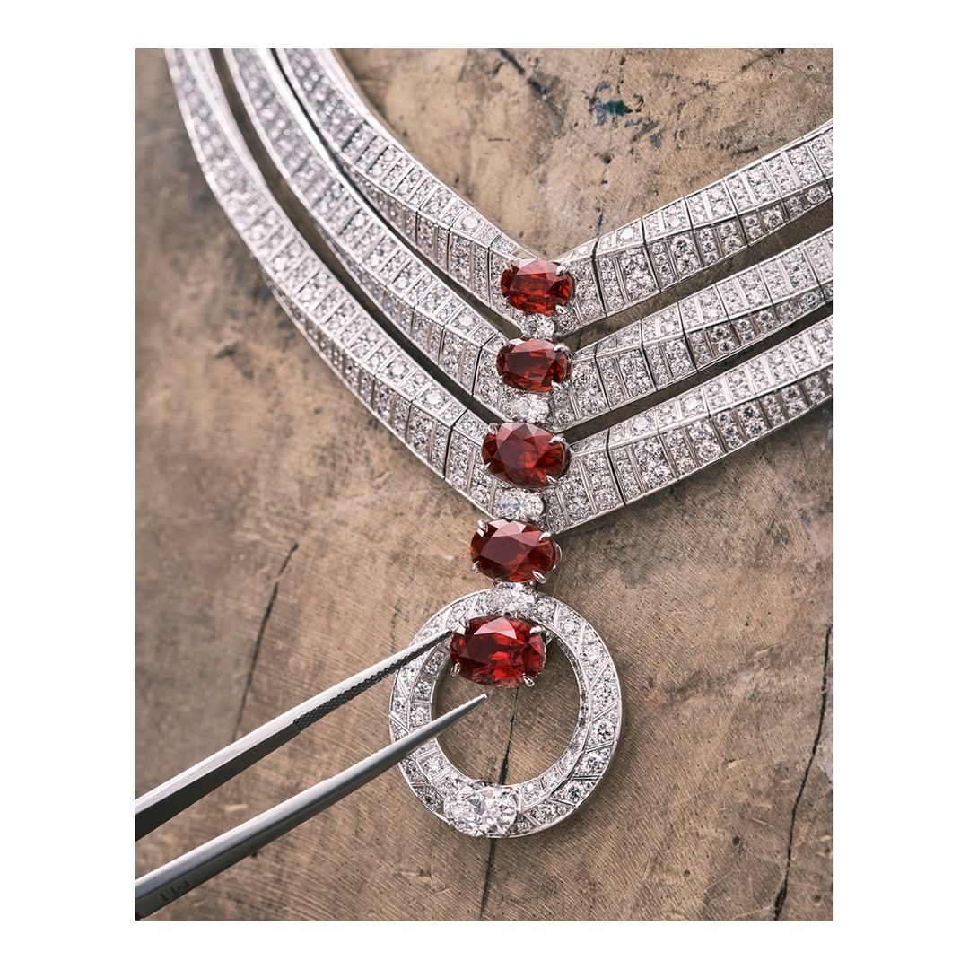 Close-up of a diamond and garnet necklace being assembled with tweezers, set against a textured wooden surface, high-end jewelry.