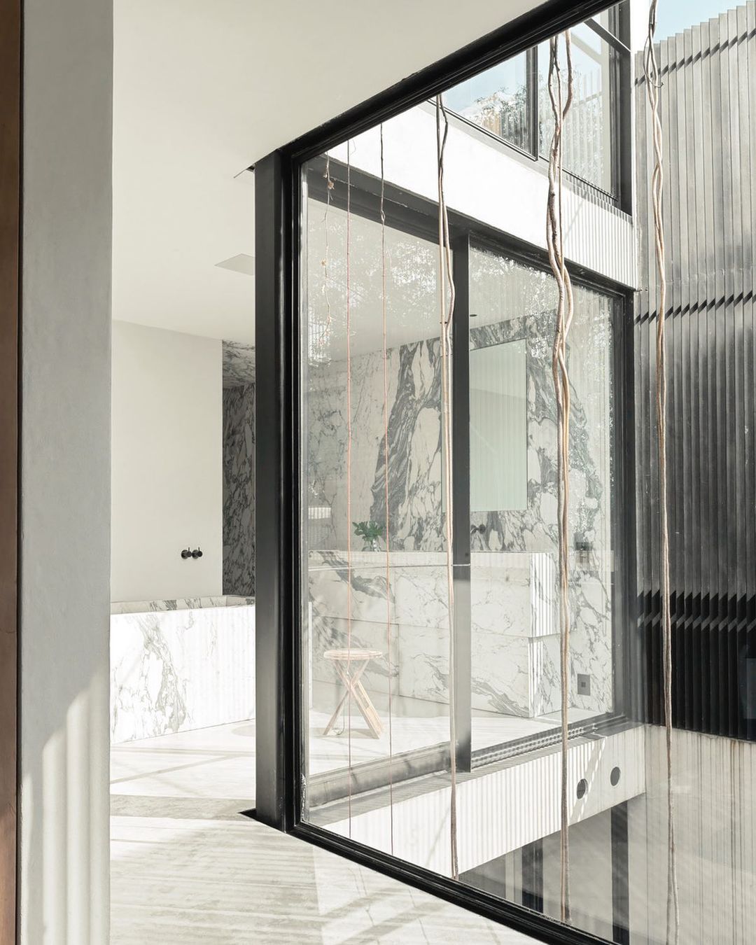 Modern bathroom interior featuring marble walls, a glass partition, and a small wooden stool, showcasing minimalist design.