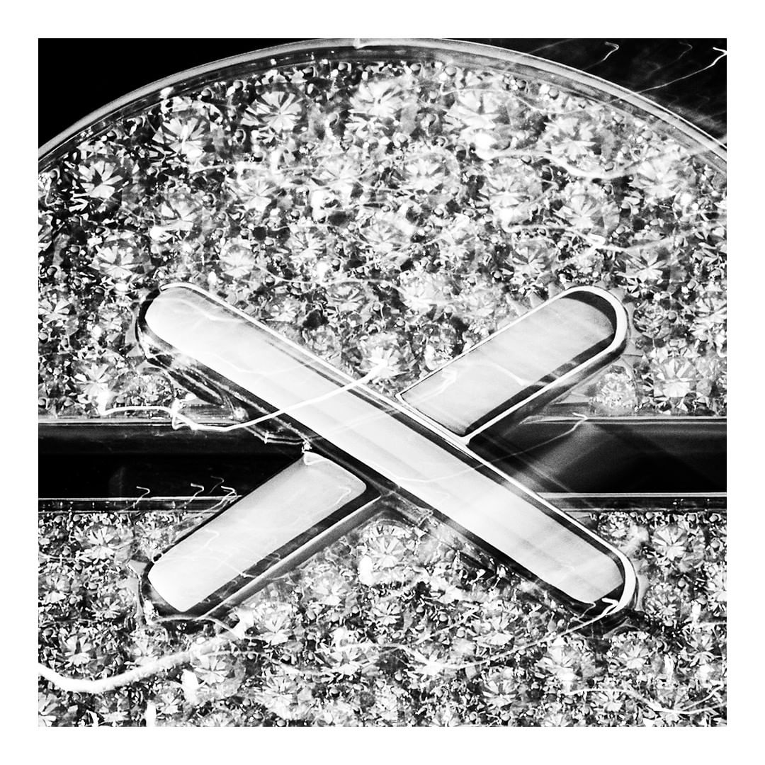 Black and white image featuring overlapping rounded-edge bars against a blurred background of gemstones, creating a textured, patterned effect.