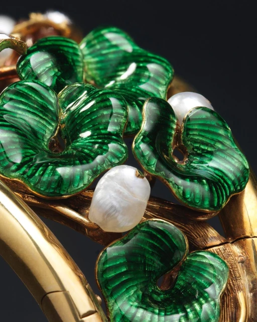 Close-up of a gold bracelet with green enamel leaves and white pearls, set against a dark background, showcasing fine jewelry.