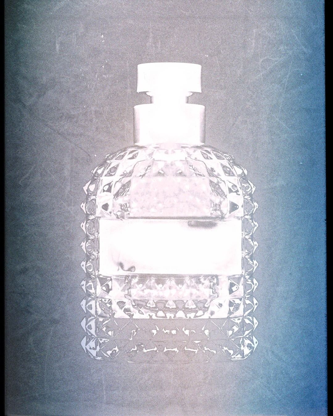 Close-up product photograph of a faceted glass perfume bottle with a textured textured surface against a dark gradient background.