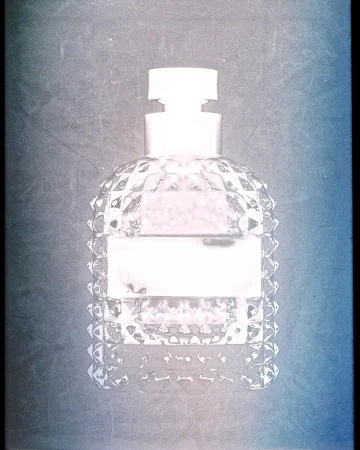 Close-up product photograph of a faceted glass perfume bottle with a textured textured surface against a dark gradient background.