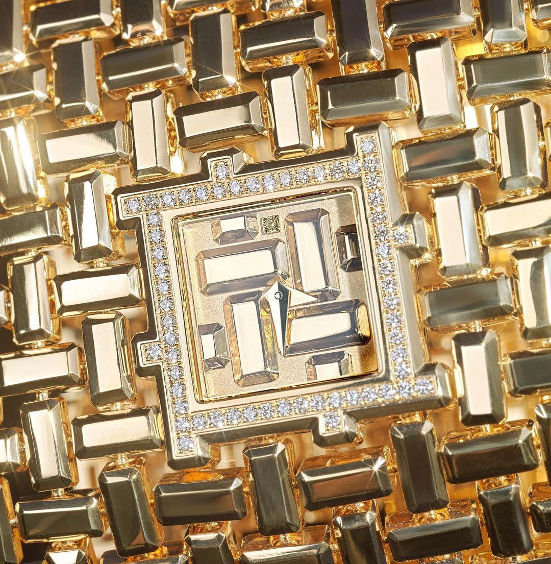 Close-up of a gold-tone wrist watch with crystal embellishments and geometric designs, set on a matching gold-tone background with more geometric shapes.