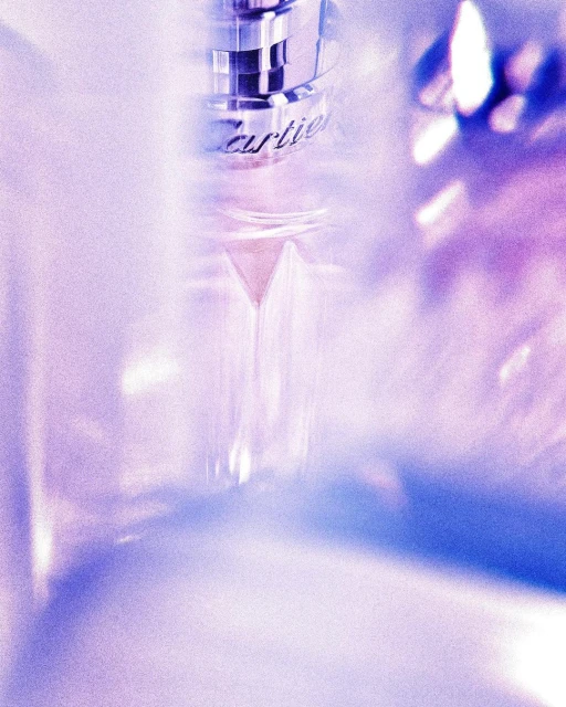 Close-up product shot of a clear glass perfume bottle with metallic silver accents, against a soft, light purple backdrop.