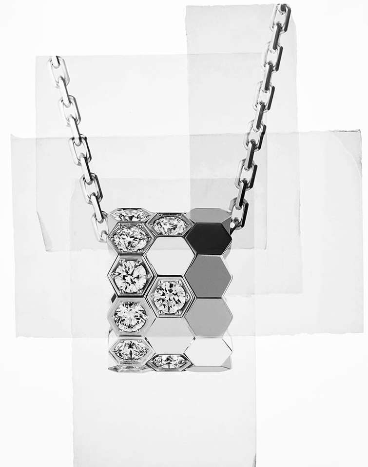 Silver necklace with a hexagonal pendant featuring diamond accents, displayed against an abstract background of white paper fragments.