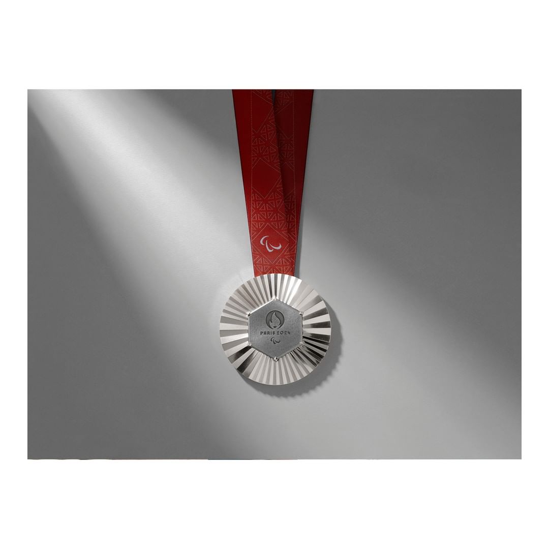 Silver medal with a red ribbon rests on a light gray surface, illuminated by a beam of light, enhancing its metallic details.