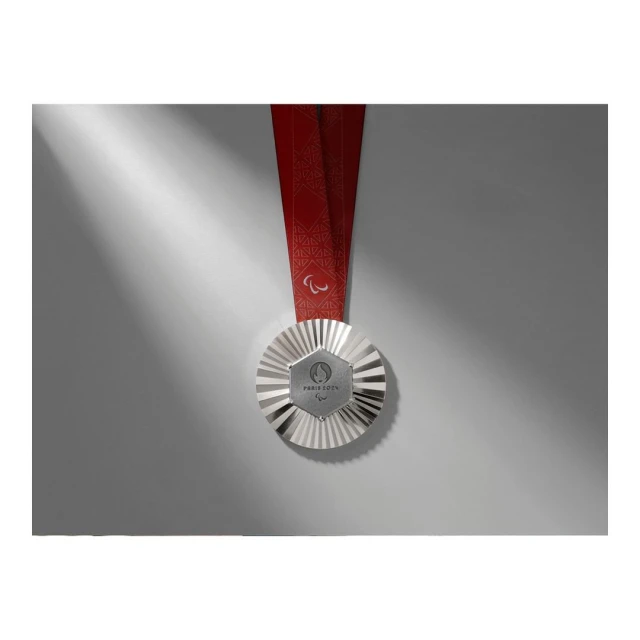 Silver medal with a red ribbon rests on a light gray surface, illuminated by a beam of light, enhancing its metallic details.