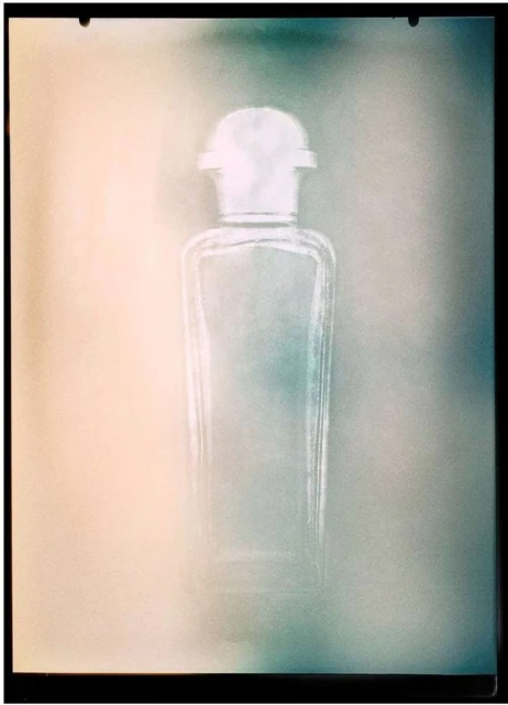 Artistic studio shot of a vintage transparent glass bottle with a white cap, set against a gradient background with teal and peach tones.