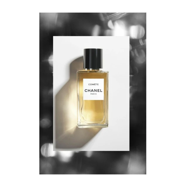 Elegant still life of a Chanel 'Comete' perfume bottle on a white surface, set against a bokeh-lit background creating a luxurious, artistic product shot.