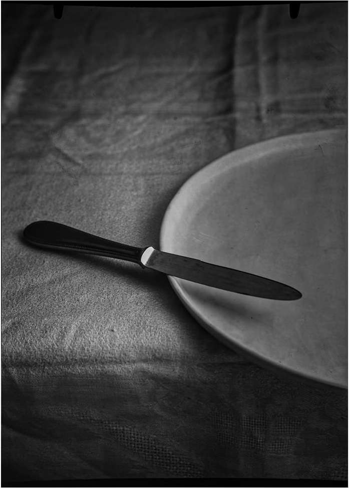 Monochrome still life of a dinner knife resting on a plate atop a draped tablecloth, showcasing minimalist elegance.