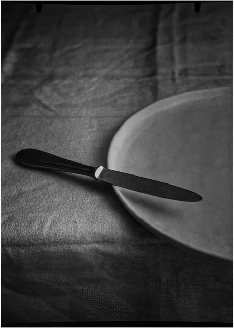 Monochrome still life of a dinner knife resting on a plate atop a draped tablecloth, showcasing minimalist elegance.