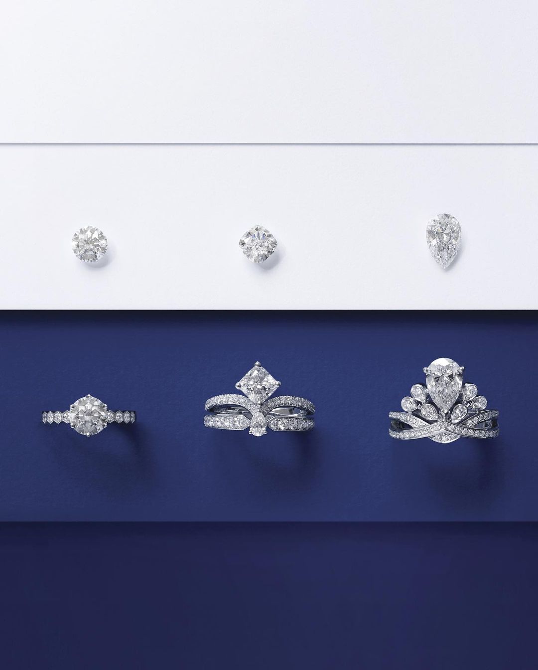 Elevated product shot of three diamond rings and three loose diamonds arranged on a split white and navy blue background.