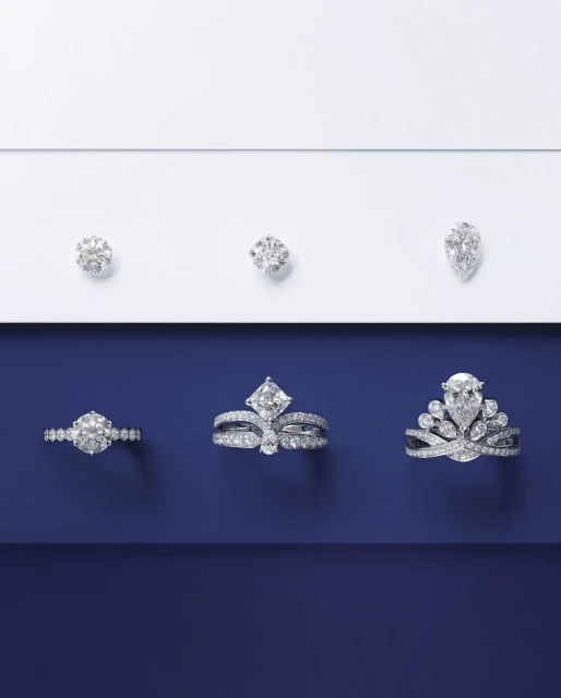 Elevated product shot of three diamond rings and three loose diamonds arranged on a split white and navy blue background.
