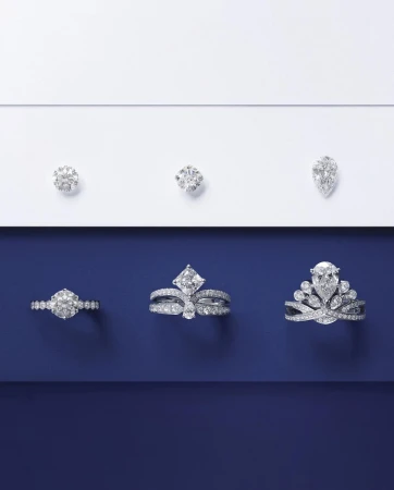 Elevated product shot of three diamond rings and three loose diamonds arranged on a split white and navy blue background.