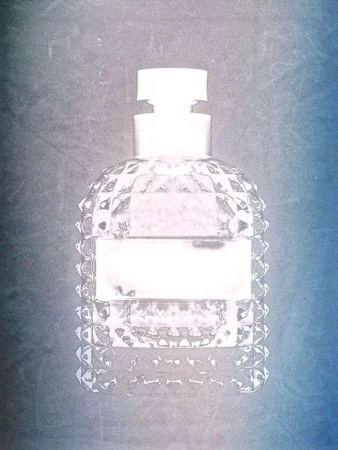 Close-up of a clear, faceted glass perfume bottle with a white cap and label against a textured blue and grey gradient background.