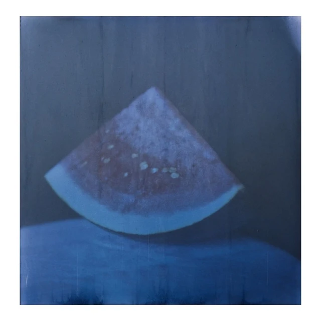 Close-up photograph of a slice of watermelon with seeds. The watermelon slice sits on a reflective blue surface.
