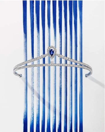 Elegant tiara with a sapphire teardrop accent, set against a backdrop of vibrant blue brushstrokes on a white surface, showcasing luxury and artistry.