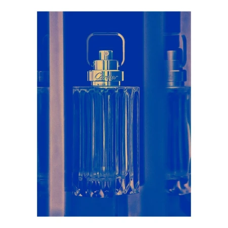 A clear glass perfume bottle with a metal handle against a vibrant blue duotone background by Thomas Deschamps.